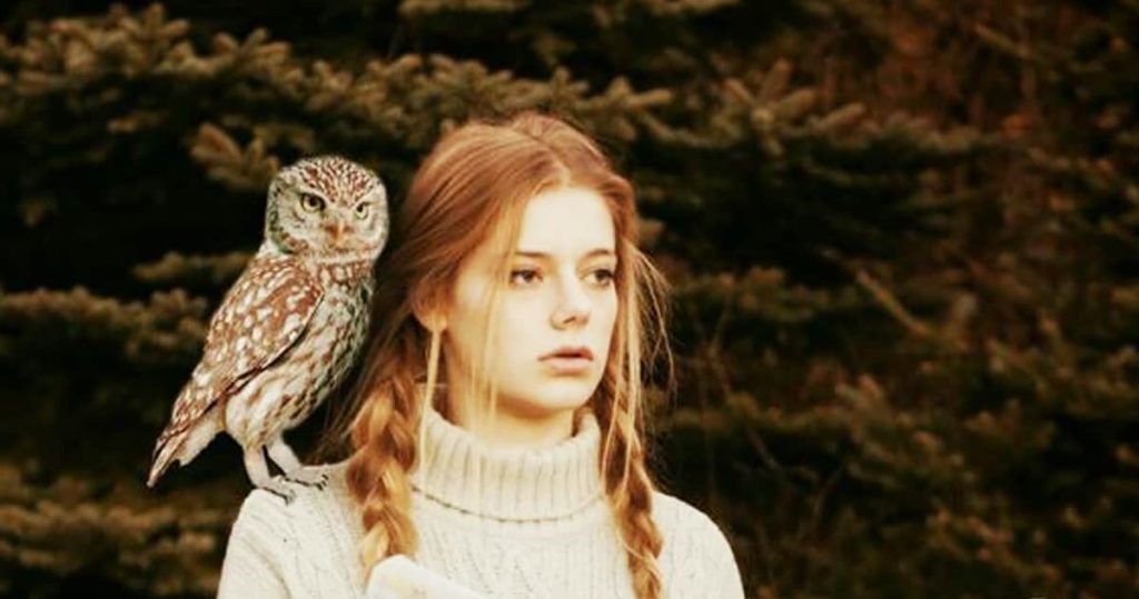 An owl stands on the woman's shoulder